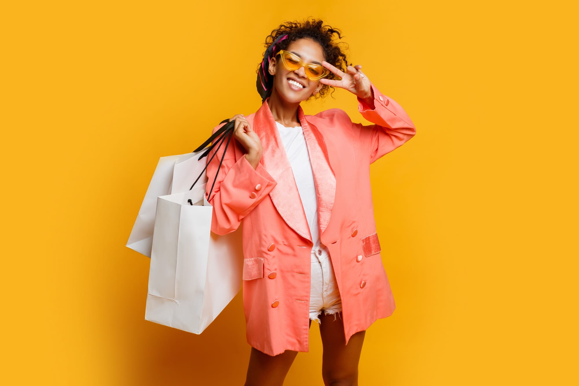 Mulher negra vestindo um blazer vermelhor segurando duas bolsas de compras brancas