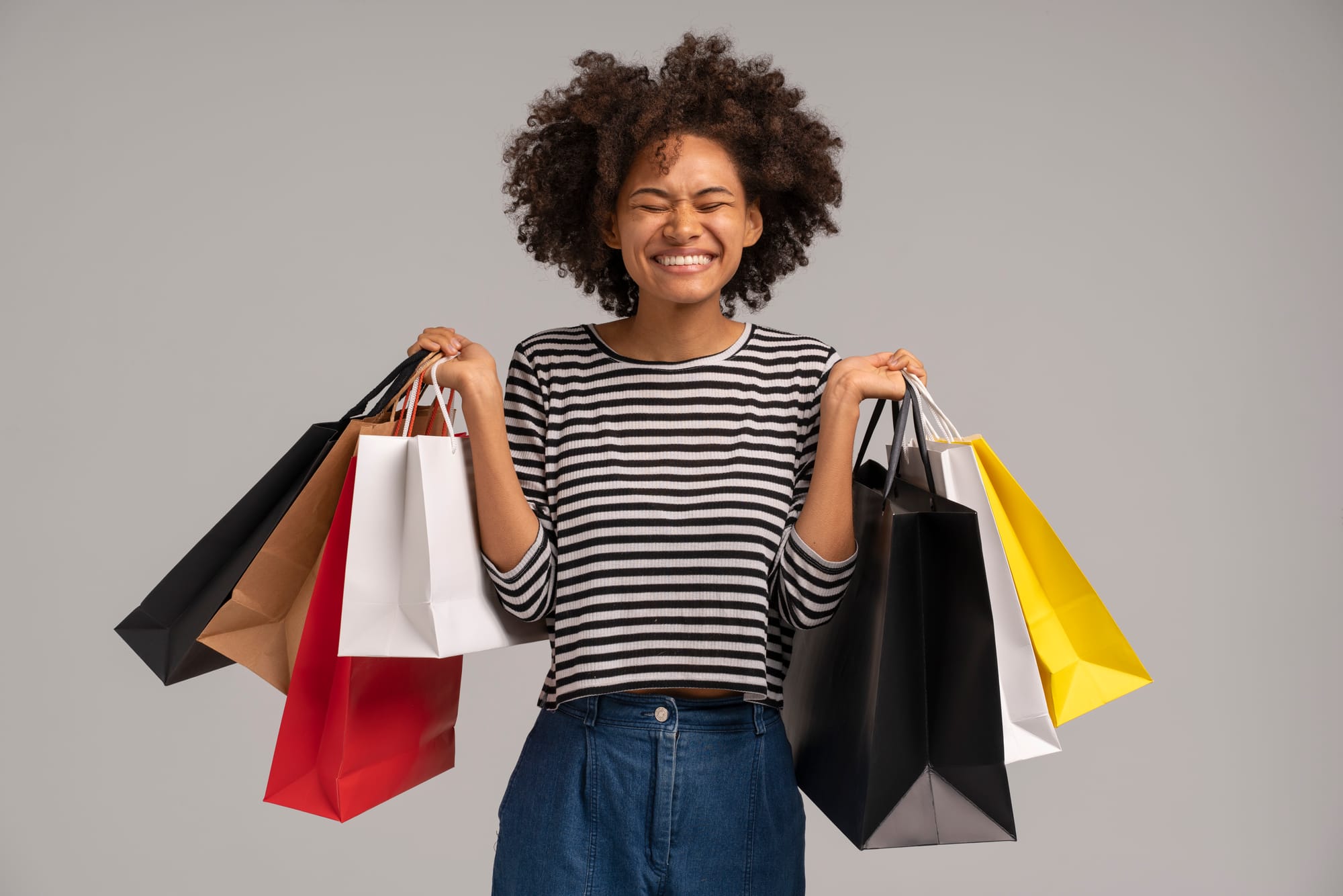 Mulher negra sorrindo e segurando diversas sacolas de compras