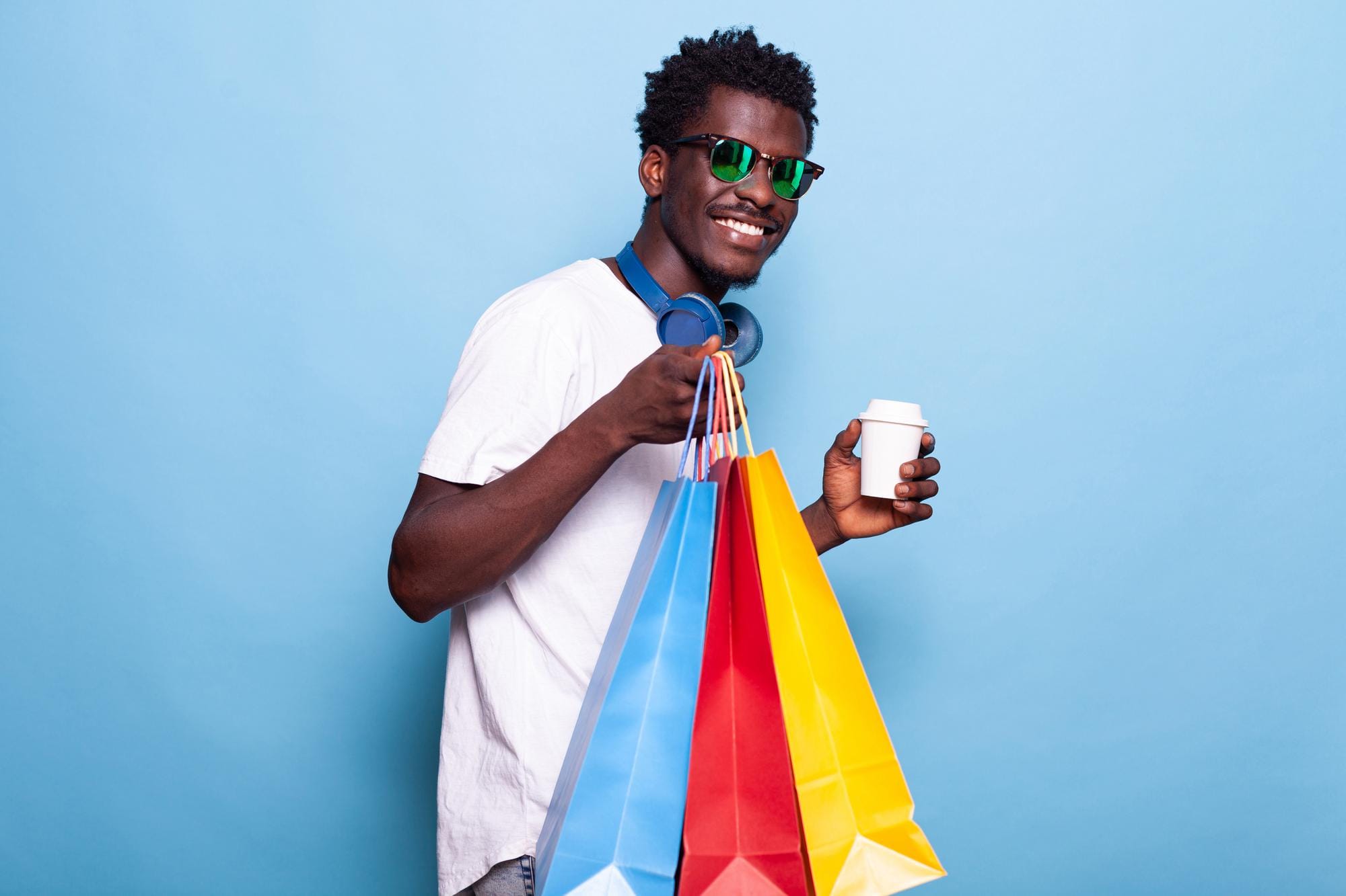 Homem negro de óculos segurando três sacolas de compras