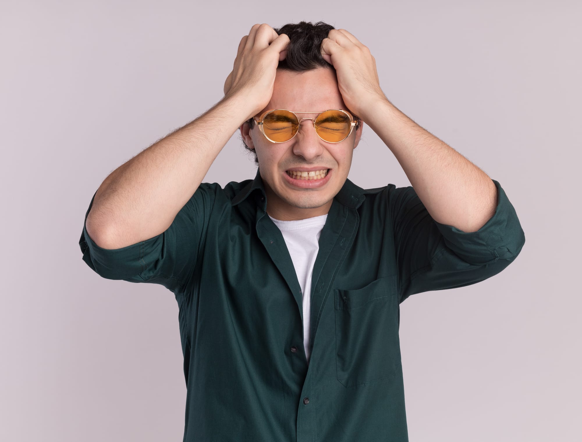 Homem  irritado  de camisa verde com as duas mão na cabeça 